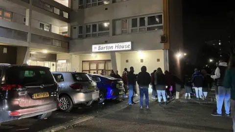 BBC People standing in the dark outside a tower block with lights on