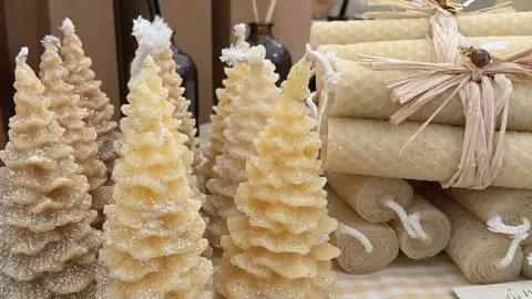 A close up of beeswax candles shaped like Christmas trees next to a small pile of beeswax candles tied together with twine