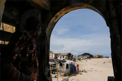 Reuters A man looks through a view at the Alpha beach, affected by an ocean surge, in Lagos, Nigeria on 21 June.