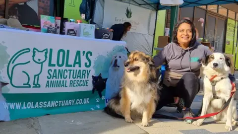 Lola's Sanctuary/Facebook Poonam Doshi with two dogs by a charity stall