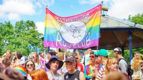 LHG Run Club People standing underneath a Left Handed Giant Run Club flag at Bristol Pride