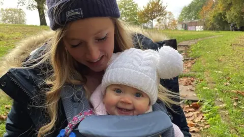 Charlotte Smart Charlotte and Maya in a pappouse both wearing woolly hats and smiling on a walk