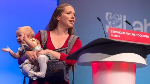 Catherine Atkinson, the Labour parliamentary candidate for Erewash, holds her nine-month-old daughter as she addresses delegates at the Labour Party conference in Brighton