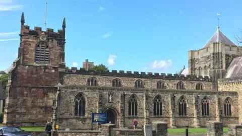An exterior view of Bangor Cathedral, it is a clear day and there are two people in the foreground of the picture, one walking towards the front door of the cathedral
