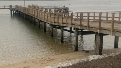 Timber pier running from shingle beach out to water it has A "T-shaped" end.