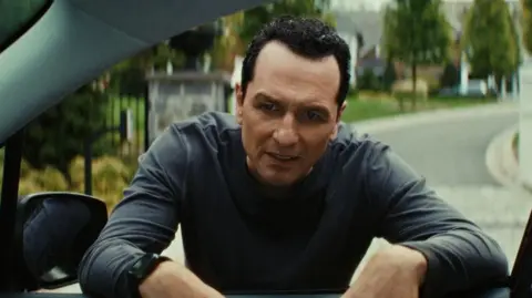 The Beast In Me / Netflix Matthew Rhys as Nile Jarvis in The Beast In Me peers through car window with a grimace