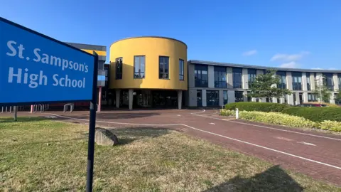 BBC A modern-looking school with colourful, yellow walls and curves. A sign says St Sampson's School.