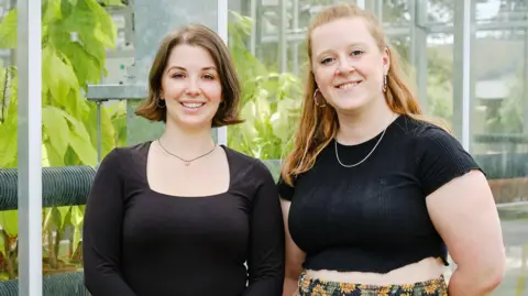 Albotherm Molly Allington and Dr Sian Fussell stand next to a greenhouse with plants in the background