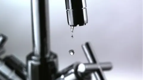 BBC A close-up of a chrome kitchen tap with a few drops of water dripping out