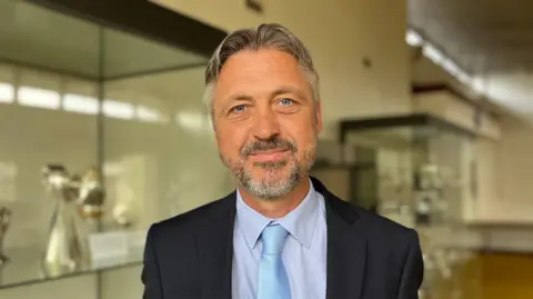 A man with a beard in a jacket and turquoise tie