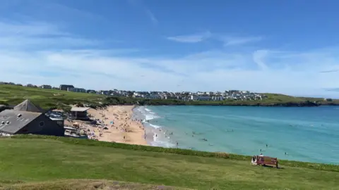 A wide sandy beach with lots of people on, and in the sea