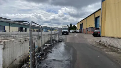 A large parking area outside a warehouse site with yellow walls.