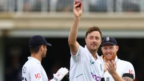 Ollie Robinson holds a cricket ball aloft and is applauded by England captain Ben Stokes
