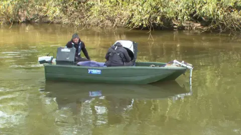 Two police officers sit on a green boat on a river