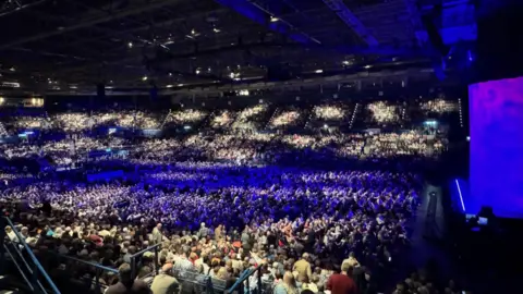 A wide photo of an indoor arena with many people inside.