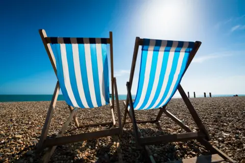 stock shot of seats on a sunny beach, two deckchairs with blue and white stripes