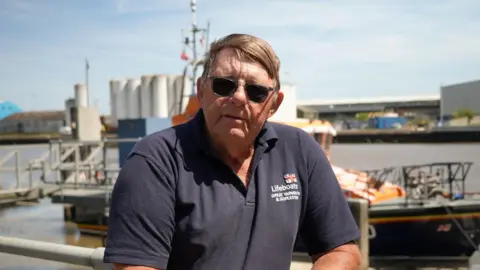 Shaun Whitmore/BBC A man wearing a black polo shirt. He is standing on Gorleston Pier. He is wearing black sunglasses and has brown hair that has been combed over to one side.
