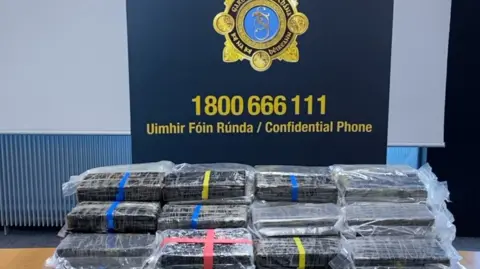 Bundles of suspected cocaine in front of a blue Gardai logo with a confidential telephone number in yellow