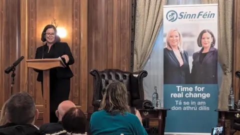 BBC  Mary Lou McDonald speaking to the press in a black suit 