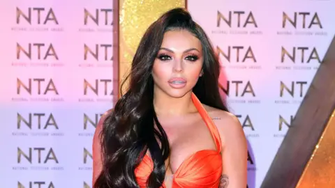 PA Media Jesy Nelson, who has long dark hair and is wearing an orange dress, posing at an awards ceremony.