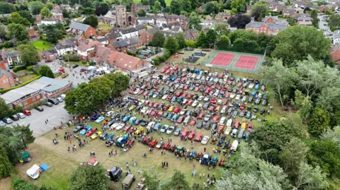 Jonathan White An aerial view of a village playing field, with cars and vehicles massed across the grass