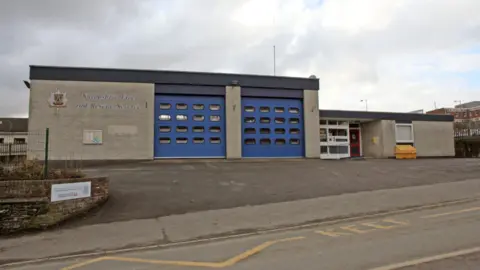Shropshire Fire and Rescue Service A fire station set back from the road with two large blue doors. The words Shropshire Fire and Rescue Service are in large letters on the building to the left of the doors on the photo.