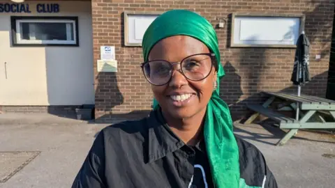 Fadumo Farah is wearing a dark shirt, green head scarf and big glasses outside a social club in Barton Hill