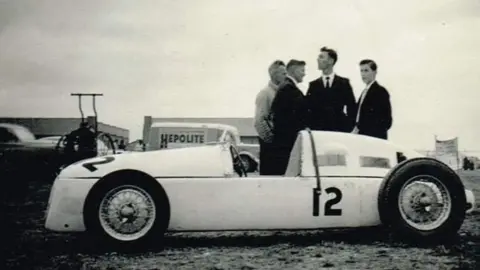 Ian Jones A black and white photograph of four men standing behind the RA4 Vanguard