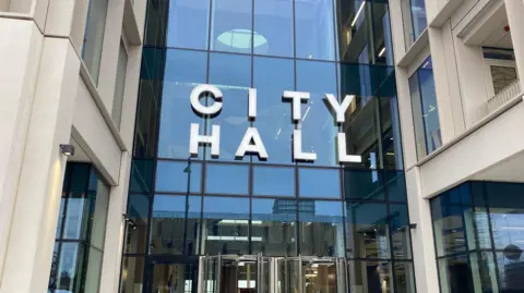 The entrance of Sunderland City Council headquarters. The sign above the glass fronted building reads "city hall". 