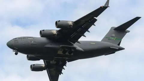 Jon Hobley/Getty Images Large grey US military transport aircraft in the air. It has a large airframe and USAF livery. The C-17A has four engines.
