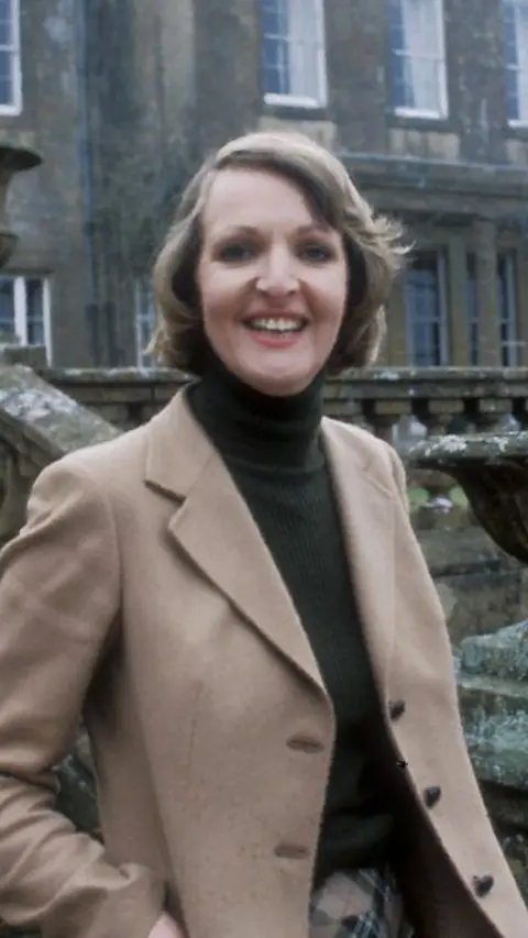 Penelope Keith standing on the steps of a country house