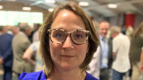 Caroline Newton, wearing tortoiseshell glasses and a blue top, looking at the camera.