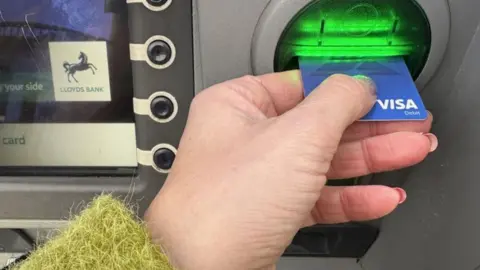 A hand putting a bank card into a Lloyds Bank ATM machine.