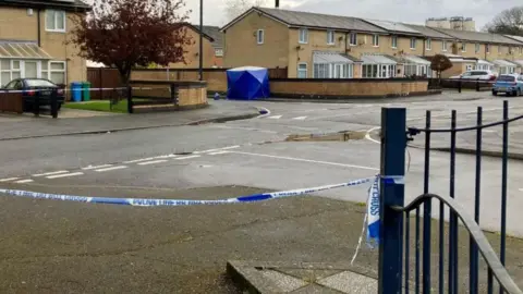 Crime scene on a residential street sealed off with blue-and-white police tape.
