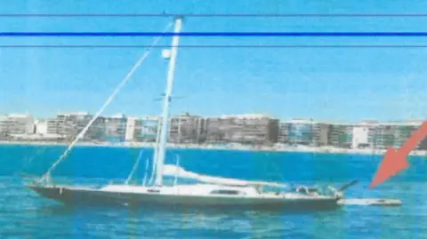Guardia Civil A grainy image of a long white and green boat on bright blue water. Tall apartment blocks are pictured on land in the background.