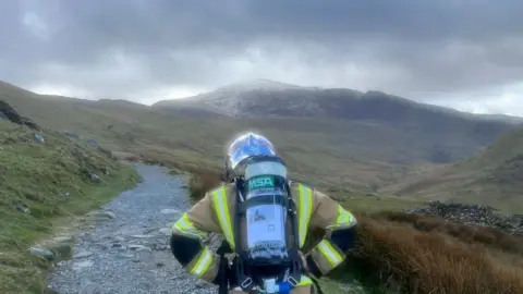 Lou Needham A firefighter in full uniform walking up a mountain