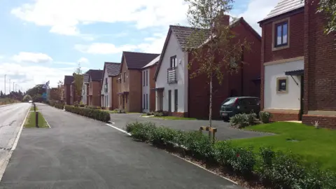 Leicester City Council Ashton Green development, near Beaumont Leys, in Leicester. A row of detached houses are located just off the right-hand side of the road.