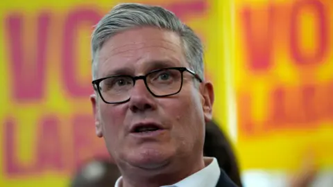 Sir Keir Starmer pictured wearing a dark suit with Labour placards in the background