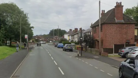 Residential road with parked cars on the right and a bus stop on the left