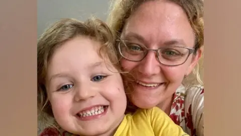 Athena Rowley cuddling her son Robert as they take a selfie together. She is wearing glasses and has curly hair while he wears a yellow t-shirt.