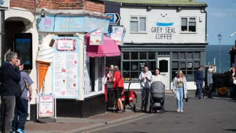 Getty Images People walk along a street and pass an ice cream parlour