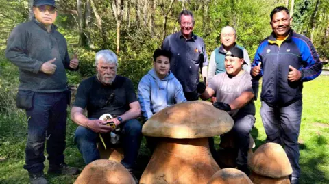 National Highways A group of men stand in a woodland area alongside large wooden toadstools.
