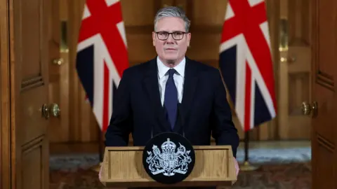 Sir Keir Starmer stands at a lectern in Downing Street flanked by two Union Jacks.