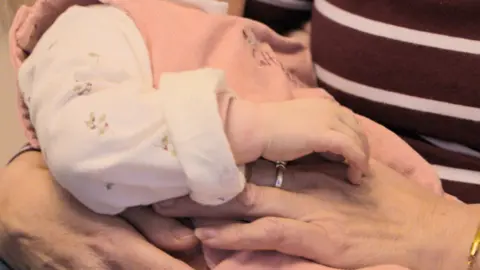 Parents And Children Together (PACT) A baby wearing a pink outfit being held by an adult 