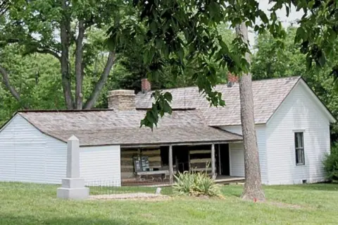 Jesse James Museum The white-washed wooden farmhouse in which he and brother Frank lived as youths. In the foreground, a fenced-off white obelisk headstone marks the original grave of Jesse James 