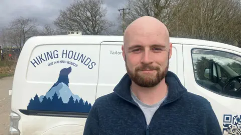 Photograph of James Cottam, who runs the Hiking Hounds dog walking business in Hollingworth. He is pictured in front of his van.