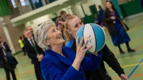Catherine Connolly holding a white and blue basketball in a sports hall. 