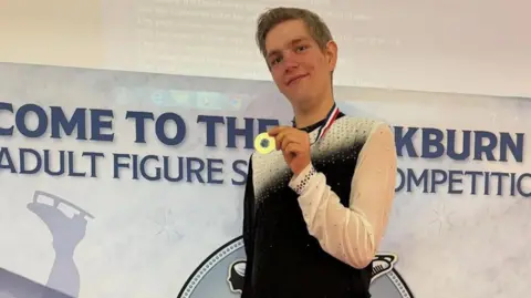 Provided Charlie holding up a gold medal at an ice skating competition.