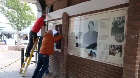 Ormskirk Community Partnership (OCP) Men erect boards celebrating Ormskirk's history on the ginnel walls.