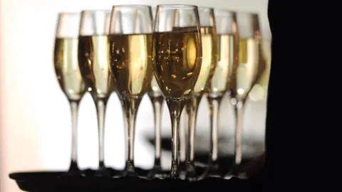 A tray full of glasses of Champagne with the arm of the waiter in silhouette. 